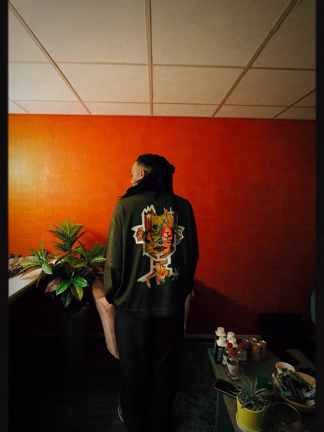 Person wearing a longsleeve shirt with a colorful design in a room with an orange wall.
